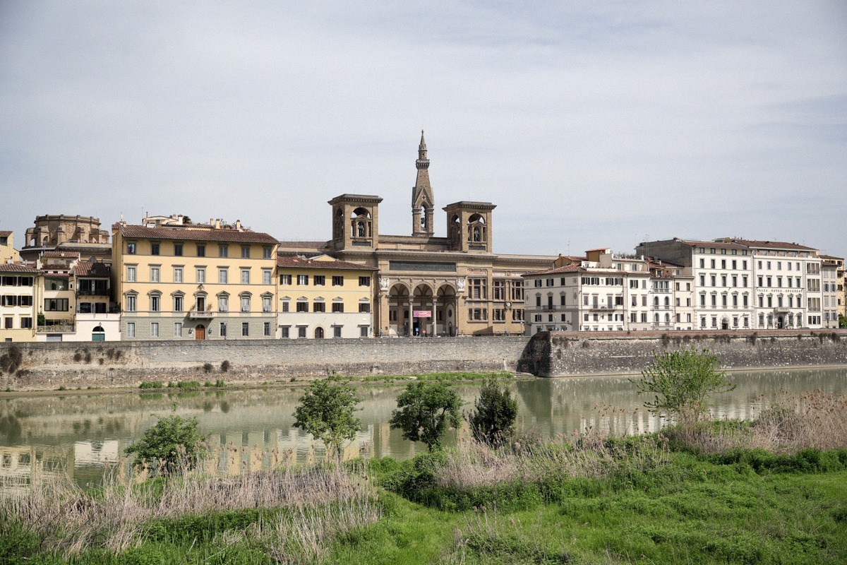 The historic skyline of Florence seen across the Arno, with riverside palaces and a church tower.
