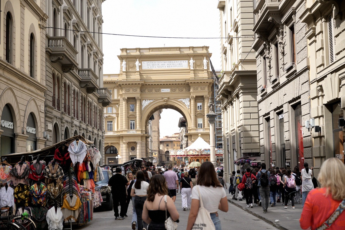 A busy shopping street leading to Piazza della Repubblica with the triumphal arch behind.