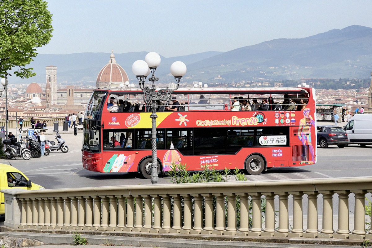 A red hop-on hop-off double-decker bus on Piazzale Michelangelo with Brunelleschi's dome behind.